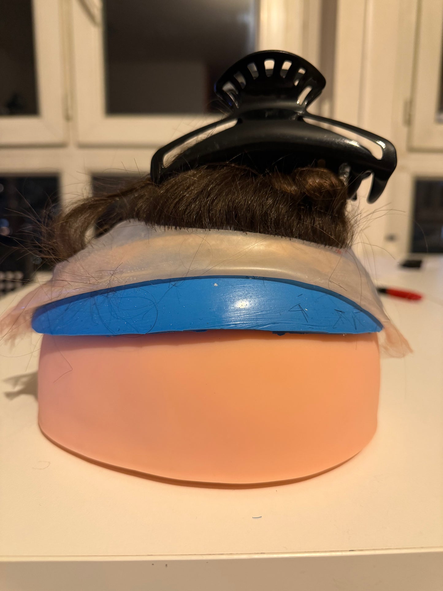 Support en caoutchouc incurvé pour l'injection de mèches de cheveux sur une micro-peau en vue de la fabrication de prothèses capillaires.